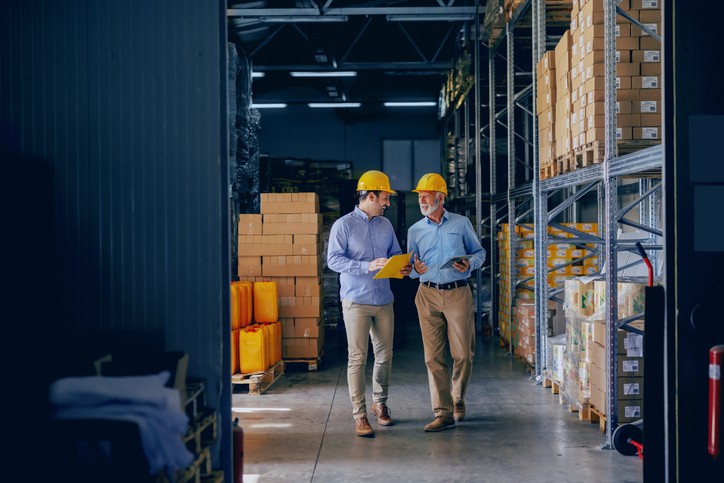 Two business partners in formal wear and with protective yellow helmets on heads walking and talking about business. 